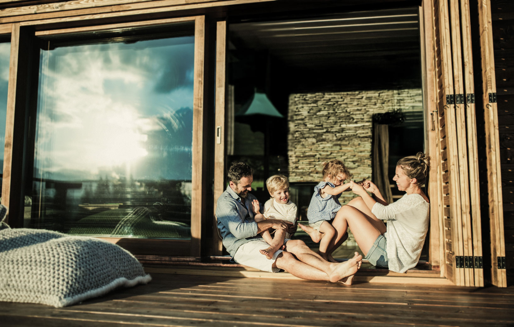 Eine Familie sitzt auf einer Terrasse, umgeben von großen Fenstern und Sonnenlicht.