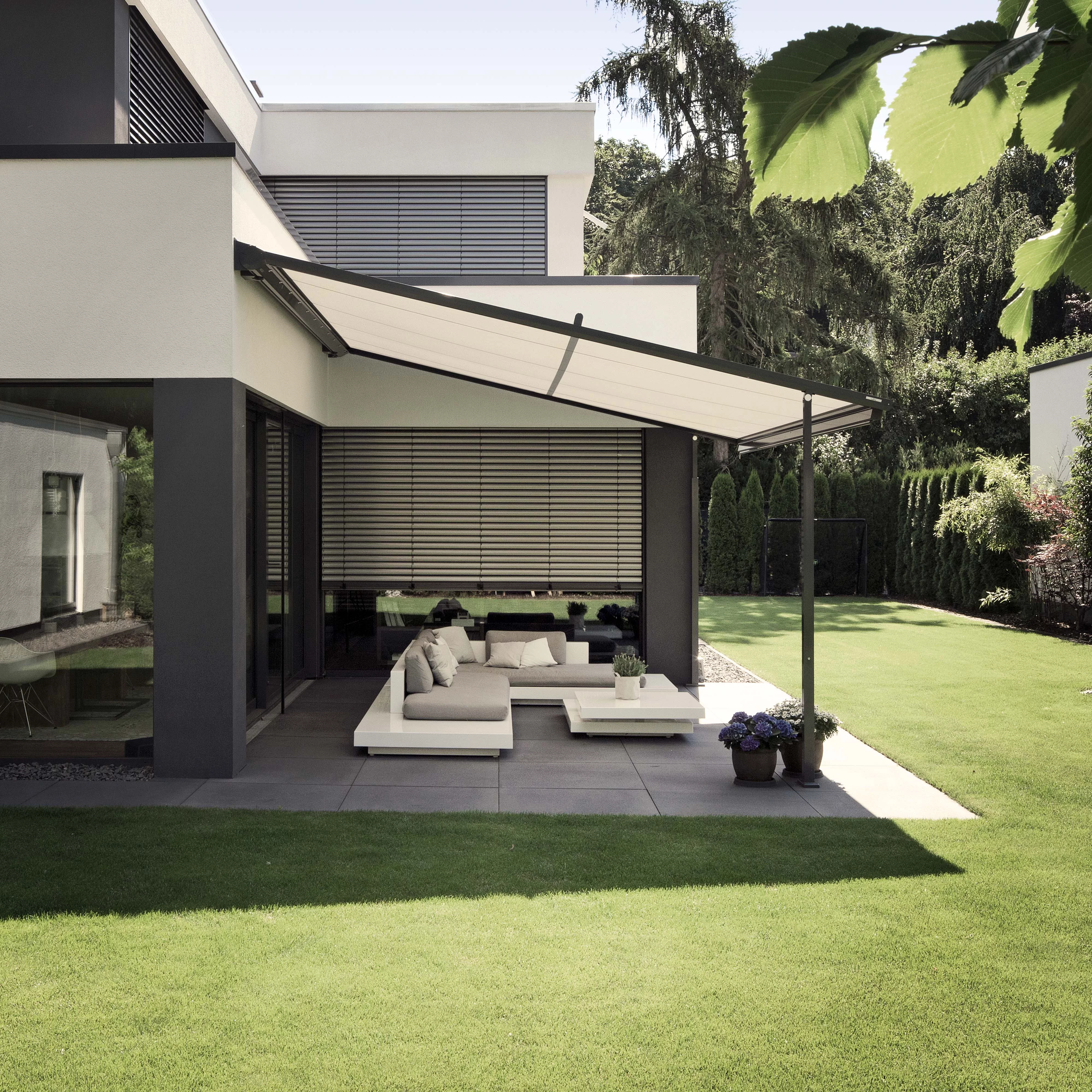 A modern terrace with a flat-roofed overhang and green grass, featuring a minimalistic seating arrangement.