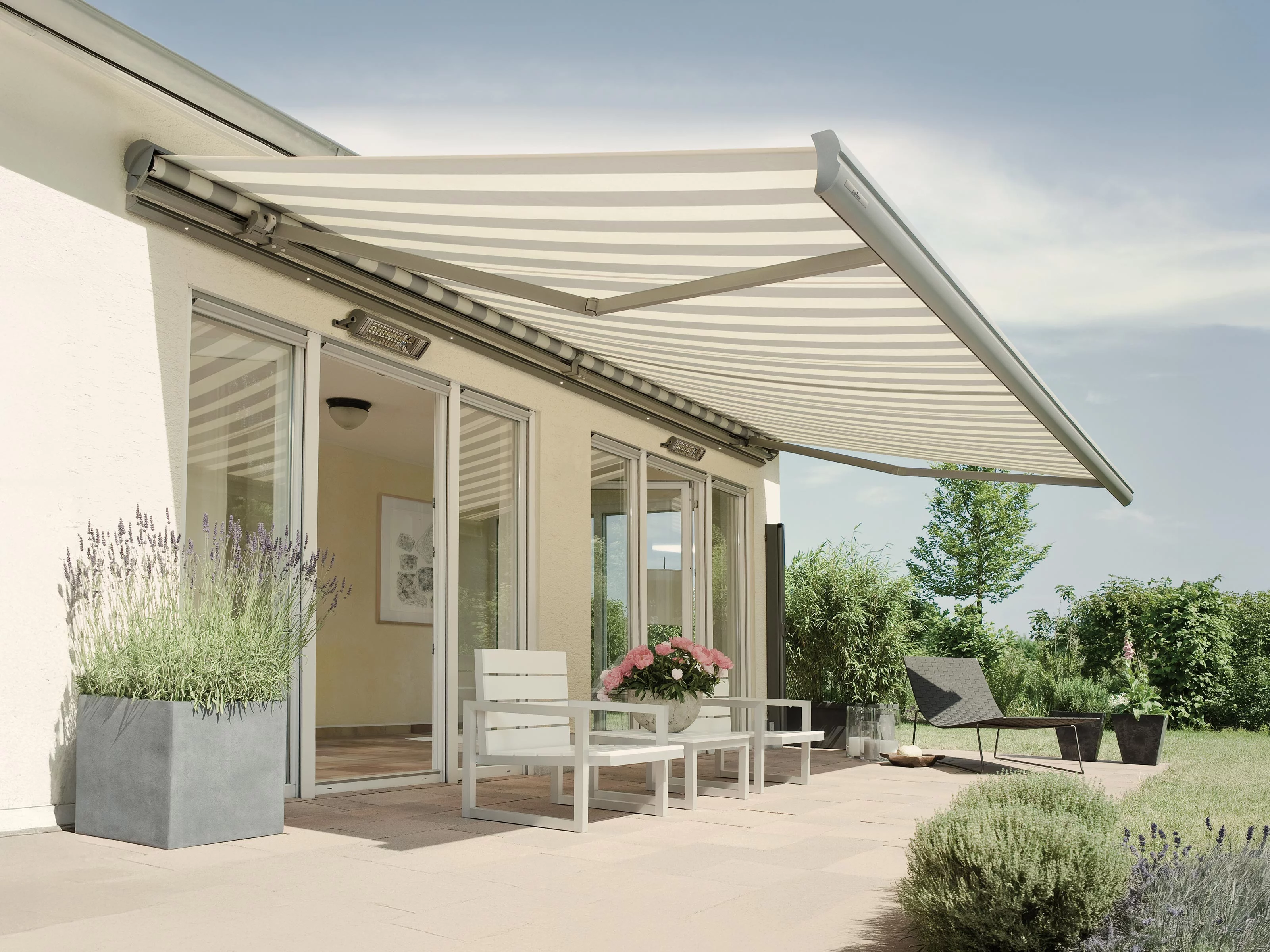 Een bouwstijl met een markise boven een terras, omringd door planten en een groene tuin.