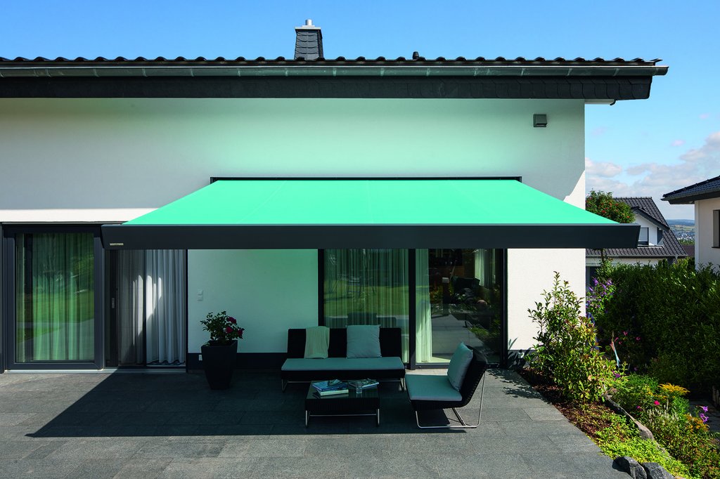 Green awning extended over a terrace area with seating and lush greenery in the background. Green awning extended over a terrace area with seating and lush greenery in the background.