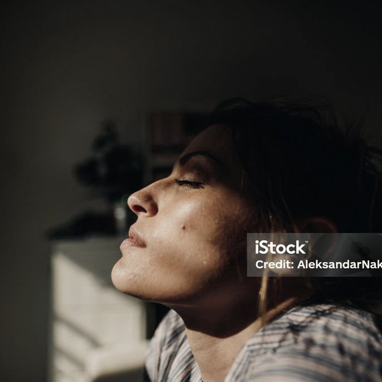 Frau mit geschlossenen Augen, die das Licht genießt, im Hintergrund eine dunkle Silhouette.