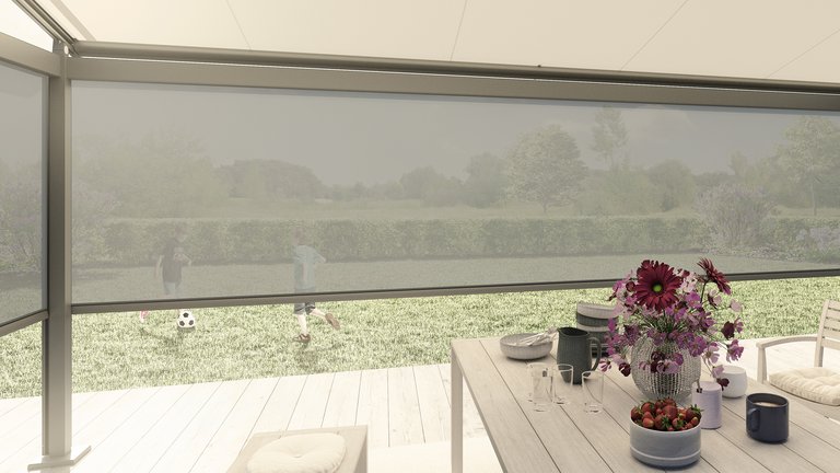 Sicht auf eine Terrassensituation mit Blumen, einem Tisch und einer Überdachung im Hintergrund. Dominante Farben: Grün und Beige.