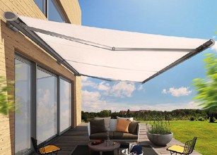 Markise in hellem Design über einer Terrassensituation mit Sitzmöbeln und Pflanzen im Hintergrund. 