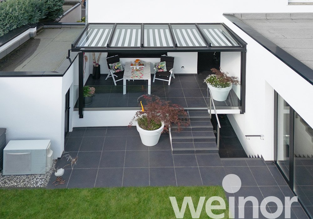 Terrassensituation mit Überdachung, hellen Pflanzkübeln und grauem Belag.