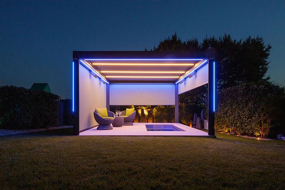 Moderne Überdachung mit LED-Beleuchtung, zwei Sitzmöbeln und Pool in einer grünen Umgebung bei Nacht. Moderne Überdachung mit LED-Beleuchtung, zwei Sitzmöbeln und Pool in einer grünen Umgebung bei Nacht.