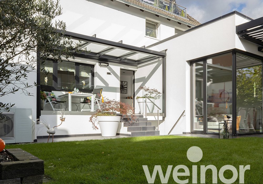 Moderne Terrassensituation mit Überdachung, hellem Gebäudebereich und grünem Rasen.