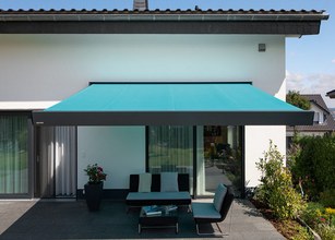 Eine blaue Markise über einer Terrassensituation mit Möbeln und Pflanzen im Hintergrund. 