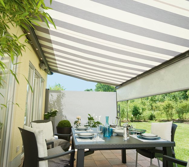 Een terras met een brede gestreepte zonnescherm en een eettafel onder een fraaie overkapping. 