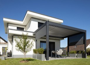 Modernes Haus mit Überdachung, Terrassensituation und klaren Linien vor blauem Himmel. 