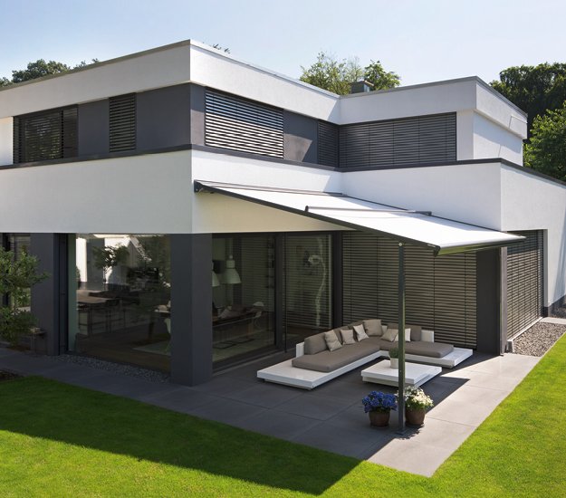 Moderne villa met een plat dak, glazen schuifwanden en elegante zonwering in een groene omgeving. 