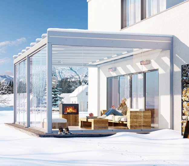 Een moderne wintergarten met glaswanden en een gezellige zithoek, omringd door sneeuw. 