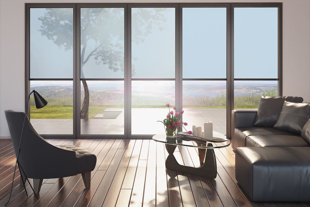 Intérieur moderne avec de grandes fenêtres, un fauteuil, une table basse et une vue sur un paysage extérieur.
