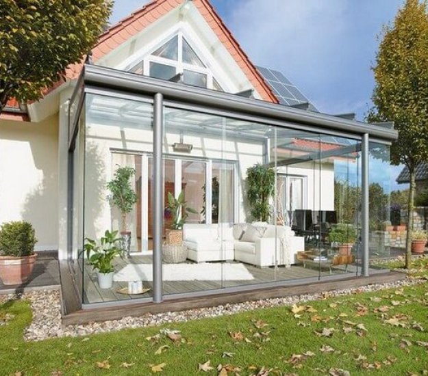 Moderne serrezonnescherm met glas en een rustige, groene terrassensituatie eromheen. 