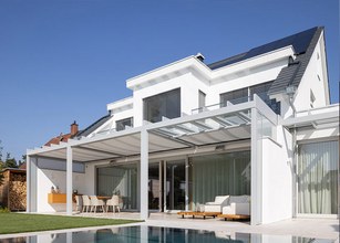 Moderne, helle Fassade eines Hauses mit Glas-Schiebewänden und Überdachung. 