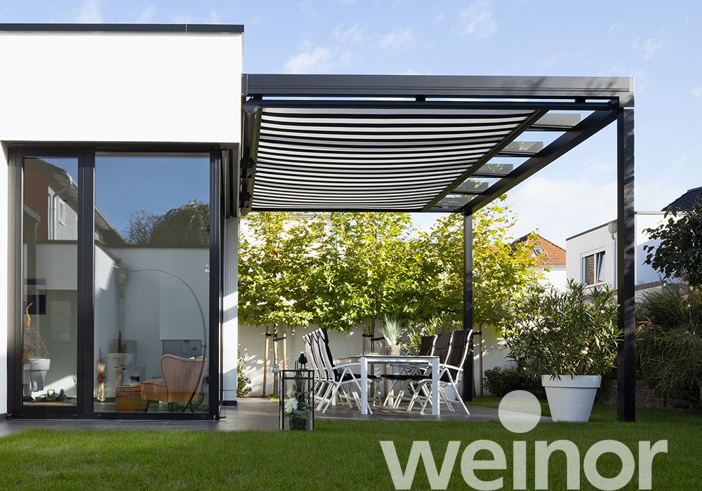 Moderne Überdachung mit Glas-Elementen und Terrassensituation vor einem hellen Haus und grünem Rasen.