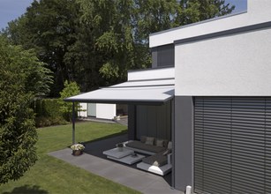 Moderne woning met een witte markies en een terras in een groene omgeving. 