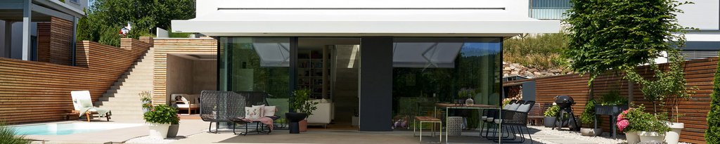 Modern outdoor terrace with glass elements and wooden features, featuring greenery and several seating arrangements. Modern outdoor terrace with glass elements and wooden features, featuring greenery and several seating arrangements.