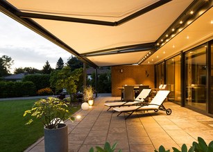 Terrassensituatie met een ruime overkapping, loungesets en sfeervolle verlichting onder een avondhemel. 