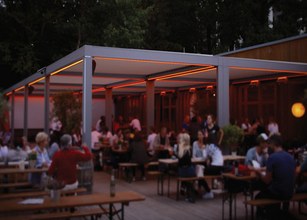 Geselliges Beisammensein unter einer Überdachung mit orangefarbener Beleuchtung und Holz-Terrassensituation. 