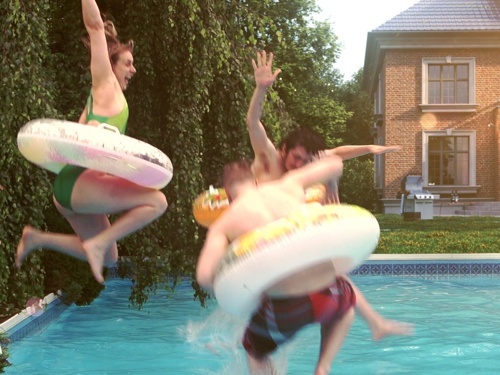 Spritzendes Wasser, vier Personen springen mit Schwimmringen in ein Poolumfeld. Spritzendes Wasser, vier Personen springen mit Schwimmringen in ein Poolumfeld.