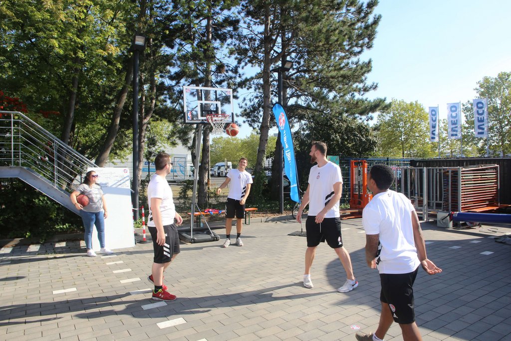 Gruppe von Personen spielt Basketball im Freien, umgeben von Bäumen und einer urbanen Umgebung. Gruppe von Personen spielt Basketball im Freien, umgeben von Bäumen und einer urbanen Umgebung.
