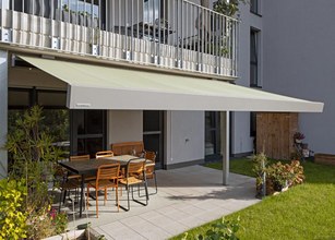 Markise in sanftem Grün über einer Terrassensituation mit Gartenmöbeln und Pflanzen. 