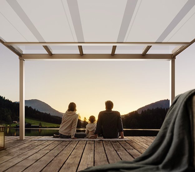 Een gezin zit onder een overkapping en kijkt naar een zonsondergang over de bergen. 
