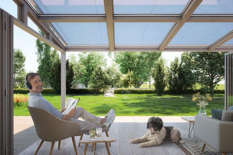 Un espace de vie en extérieur avec des surfaces en bois, des canapés et un ciel bleu à travers un toit. Un espace de vie en extérieur avec des surfaces en bois, des canapés et un ciel bleu à travers un toit.