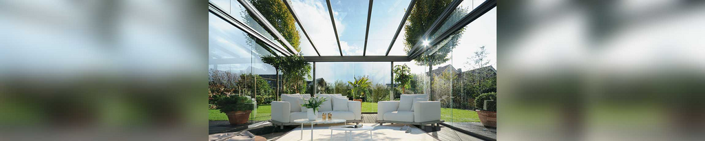 Moderne Terrassensituation mit Glas-Schiebewänden und eleganten Möbeln unter einem transparenten Dach. Moderne Terrassensituation mit Glas-Schiebewänden und eleganten Möbeln unter einem transparenten Dach.