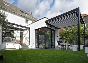 Moderne Architektur mit Überdachung, großen Fenstern und einer Terrassensituation im Grünen. 