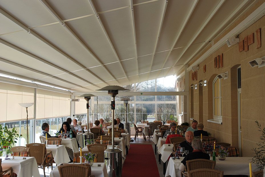 Indoor restaurant with tables, chairs, plants, and a sloped ceiling. Natural light illuminates the space. Indoor restaurant with tables, chairs, plants, and a sloped ceiling. Natural light illuminates the space.
