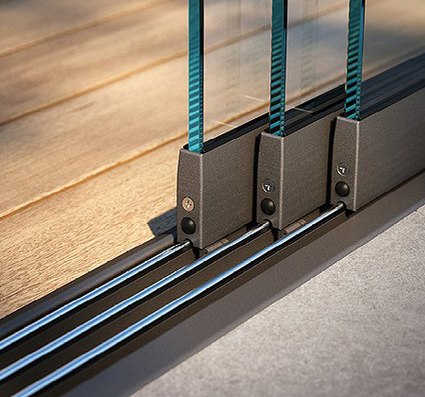 Details van een glazen schuifwand met metalen rails en houten vloer.
