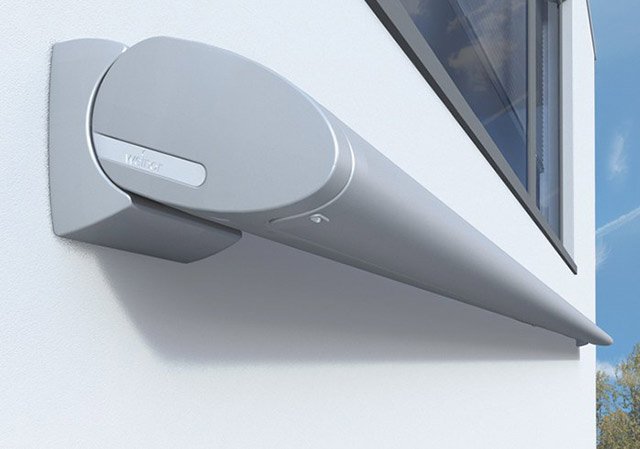 Sleek grey awning mounted on a white wall, featuring a modern, elongated design. Sleek grey awning mounted on a white wall, featuring a modern, elongated design.