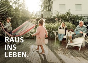 Familie im Freien, Kind tanzt zwischen Gartenmöbeln und Hängematte, entspannte Atmosphäre. 