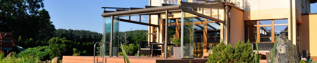Modern glass structure with an outdoor terrace, surrounded by greenery and blue sky. Modern glass structure with an outdoor terrace, surrounded by greenery and blue sky.