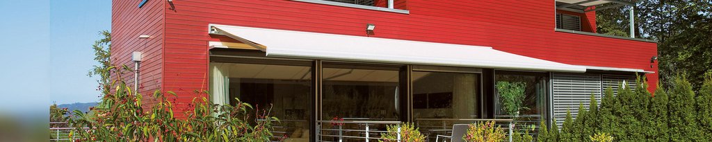Maison moderne avec une façade rouge et une terrasse, marquise déployée au-dessus. Maison moderne avec une façade rouge et une terrasse, marquise déployée au-dessus.