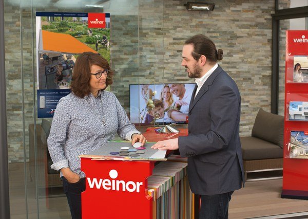 Deux personnes discutent autour d'une table, dans un espace moderne avec des brochures et un écran. Deux personnes discutent autour d'une table, dans un espace moderne avec des brochures et un écran.