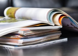 Stapel von Zeitschriften in verschiedenen Farben und Formaten auf einer dunklen Oberfläche. 