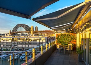 Blick auf eine Terrasse mit Markisen, Hafenblick und der Sydney Harbour Bridge im Hintergrund. 