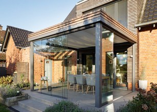 Moderne Überdachung mit Glas-Schiebewänden, grauen Stützen und anschließender Terrassensituation. 