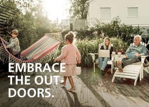 Familie im Freien mit Kindern, die spielen, und Erwachsenen auf Terrassenmöbeln. Vertraute Wohlfühlatmosphäre. 