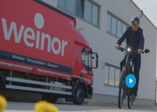 Mann in dunkelblauer Kleidung fährt auf einem E-Bike, rote Lkw im Hintergrund mit Schriftzug "weinor". 