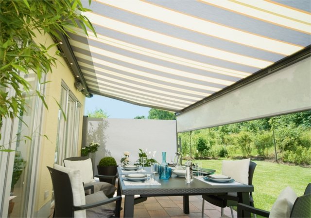 An outdoor dining area under a striped awning with a table set for a meal. An outdoor dining area under a striped awning with a table set for a meal.