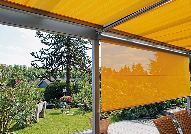 Sonnenschutz in Gelb mit Markisenkasten, Blick auf eine grüne Gartenlandschaft. Sonnenschutz in Gelb mit Markisenkasten, Blick auf eine grüne Gartenlandschaft.