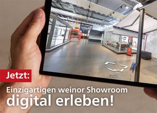 Hand, die ein digitales Tablet hält, mit einer Ansicht eines modernen Showrooms im Hintergrund. 